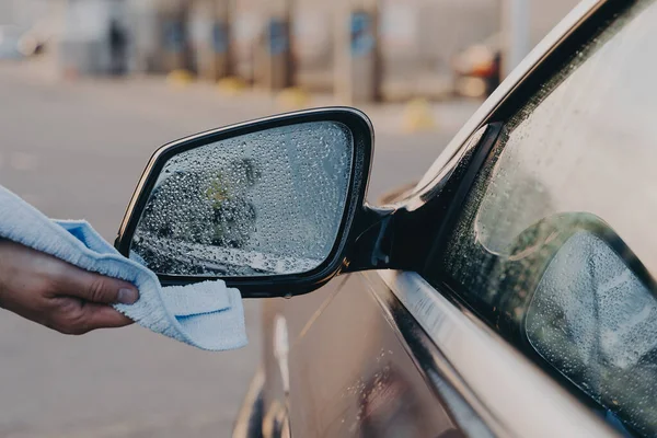 Muž ruční čištění auta venku s hadrem, otírání vody s mikrovláknitou látkou na bočním zpětném zrcátku — Stock fotografie