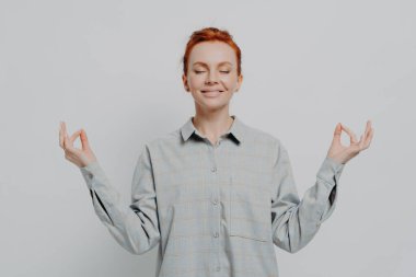 Sakin kızıl saçlı kadın, kareli gömlekli, elleri ve gözleri kapalı meditasyon yapıyor.