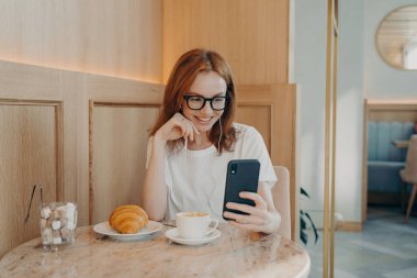 Kulaklıklı genç, pozitif saçlı kadın kafede oturuyor ve akıllı telefondan konuşuyor.