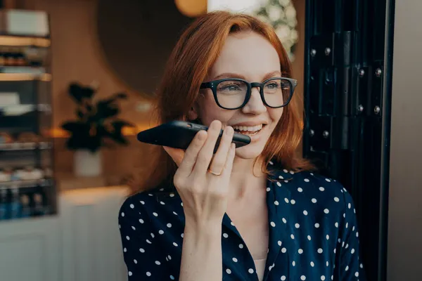 Feliz mujer de negocios sonriente habla en el teléfono celular en el altavoz mientras sale de la cafetería — Foto de Stock