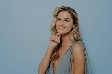 Stüdyo arka planında poz verip çenesine parmaklarıyla dokunan akşam elbisesi giymiş zarif genç bir kadın.