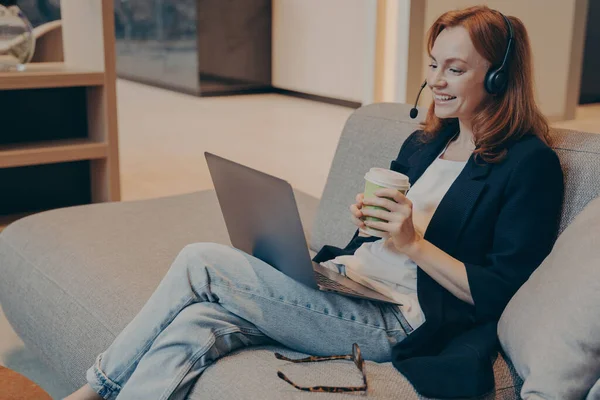 Feliz mujer milenial con auriculares y sonriendo mientras ve el curso de webinar en línea en el ordenador portátil —  Fotos de Stock