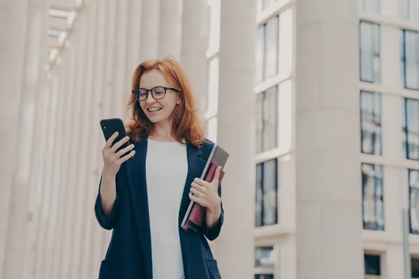 Mujer europea feliz sosteniendo el teléfono móvil y sonriendo, leyendo buenas noticias de su socio de negocios — Foto de Stock