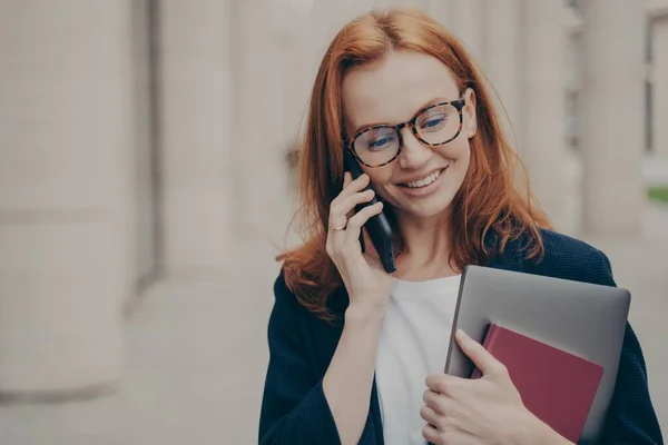 Jeune femme d'affaires caucasienne des années 30 debout à l'extérieur et parlant sur smartphone avec le client — Photo