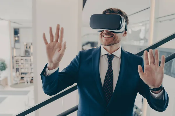 Młody podekscytowany człowiek pracownik biurowy za pomocą symulatora rzeczywistości wirtualnej w pracy, poruszając ręce w powietrzu — Zdjęcie stockowe
