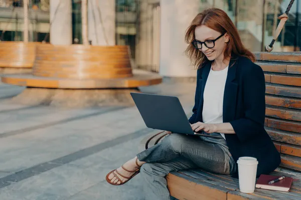 Счастливая женщина фрилансер клавиатуры на ноутбуке компьютер сидит на деревянной скамейке — стоковое фото