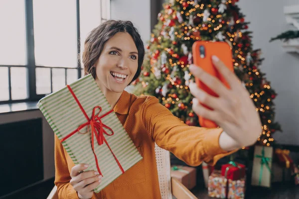 Νεαρή Ιταλίδα blogger σε απευθείας σύνδεση κάνοντας selfie με χριστουγεννιάτικο δώρο στο φόντο του χριστουγεννιάτικου δέντρου — Φωτογραφία Αρχείου