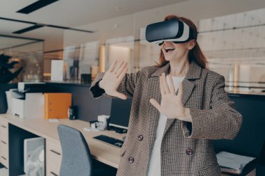 VR kulaklık takan kadın ofiste dikilirken sanal gerçeklik oyununda eğleniyor.