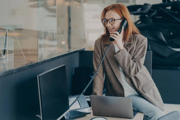 オフィスの彼女の職場に座っている間に電話で話す眼鏡の女性 — ストック写真