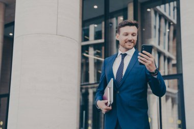 Genç yakışıklı işadamı cep telefonu kullanıyor, mesajlaşıyor ya da e-postaları kontrol ediyor, dışarıda bekliyor.