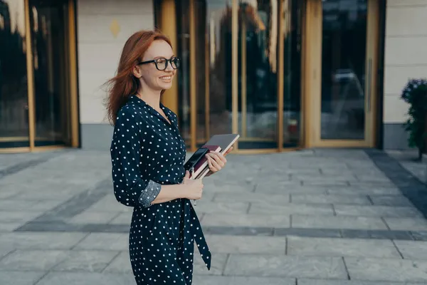 Skicklig rödhårig affärskvinna står sidled har glada uttryck bär moderna prylar — Stockfoto