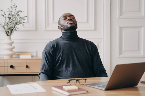 Wyczerpany pracownik biura afrykańskiego Amerykanina, siedzącego z zamkniętymi oczami, odwracającego głowę. — Zdjęcie stockowe