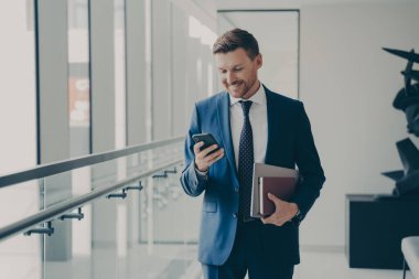 Ofisteki kahve molasında cep telefonu tutan ve gülümseyen yakışıklı yönetici.