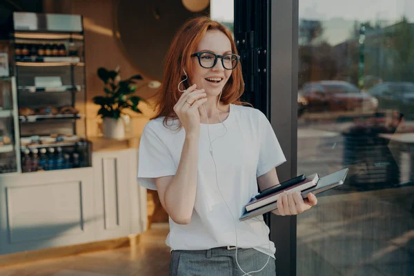 Empresária ruiva feliz com laptop na mão tendo chamada no telefone celular, deixando café — Fotografia de Stock