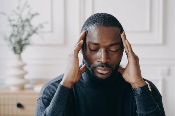 Уставший молодой афро-американский предприниматель сидит с закрытыми глазами и с руками на голове — стоковое фото