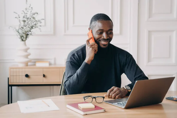 Udany afro amerykański biznesmen mający przyjemną rozmowę telefoniczną podczas pracy na laptopie — Zdjęcie stockowe