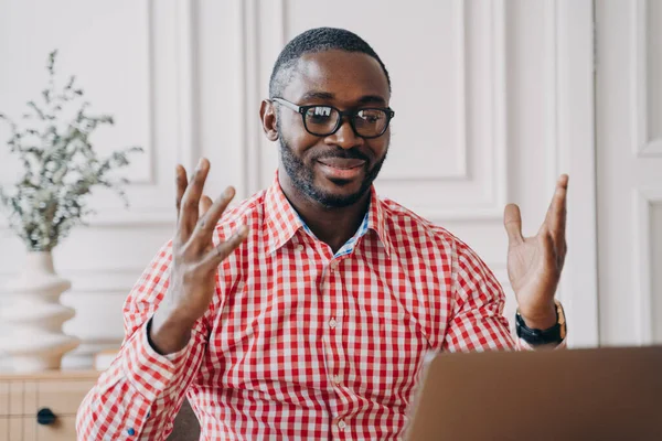 Веселый афро-американский бизнесмен в очках читает отличные новости на ноутбуке на рабочем месте — стоковое фото