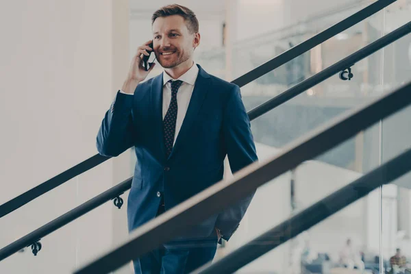Bonito empresário europeu em terno azul elegante ter conversação móvel no escritório — Fotografia de Stock