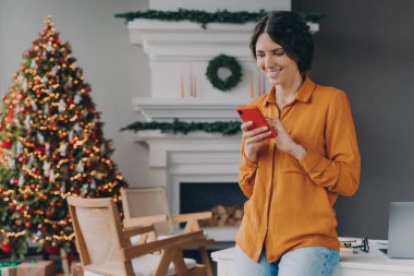 Noel tatilinde evde cep telefonuyla yazan mutlu bir kadın.