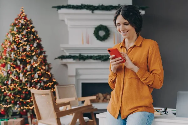 가정에서 크리스마스 때 휴대 전화로 타자를 치는 행복 한 여성 — 스톡 사진