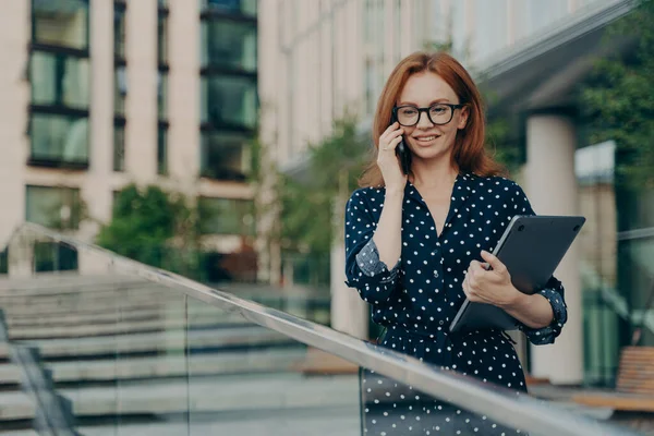 Femme rousse en vêtements à la mode a conversation téléphonique marche sur la rue près du bâtiment moderne — Photo