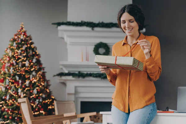 Счастливая европейская женщина открывает подарок, стоя в роскошной украшенной Рождеством гостиной — стоковое фото