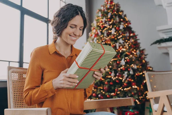 Όμορφη ευτυχισμένη Ιταλίδα που κάθεται με δώρο δίπλα στο στολισμένο χριστουγεννιάτικο δέντρο στο σπίτι — Φωτογραφία Αρχείου