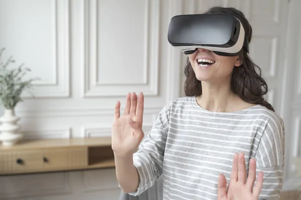 Joven mujer emocionada que usa auriculares VR interactuando con el mundo aumentado, jugando juegos en casa — Foto de Stock