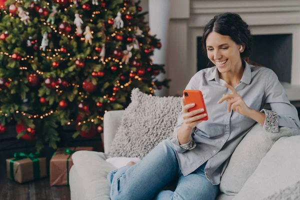 クリスマスの時間にオンラインで家族や友人と話をし、スマートフォンを保持イヤホンで幸せな女性 — ストック写真