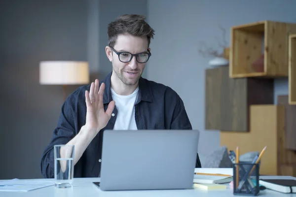 Jeune homme autrichien beau freelancer agitant la main dans le geste bonjour lors d'un appel vidéo sur ordinateur portable — Photo