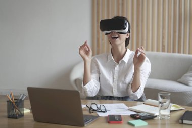 VR kulaklıklı bayan girişimci ev ofisinin masasında oturuyor ve 3D görselleştirmeyle etkileşimde.