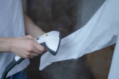 Buharlı adamın uzun kollu beyaz gömleği düzgün ütülerken çekilmiş fotoğrafı.