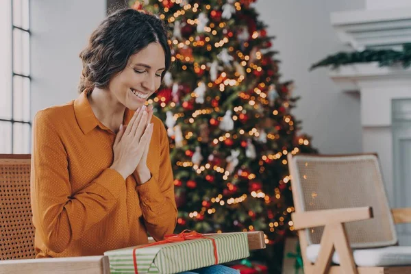 Χαρούμενη Ιταλίδα που κάθεται σε ζεστή καρέκλα με κουτί δώρου στα γόνατά της δίπλα στο εορταστικό χριστουγεννιάτικο δέντρο — Φωτογραφία Αρχείου