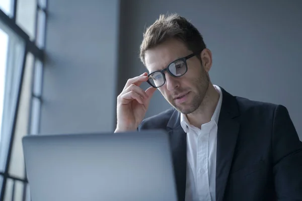 Concentré jeune homme d'affaires allemand en costume formel et lunettes regardant l'écran d'ordinateur portable — Photo