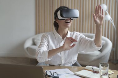 VR gözlük takan mutlu kadın ofis çalışanı iş yerinde sanal gerçeklikle etkileşime giriyor.