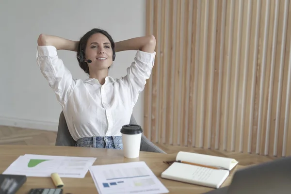 Emprendedora meditativa en auriculares sentada en posición relajada con las manos detrás de la cabeza —  Fotos de Stock