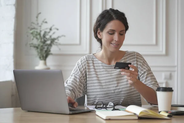 Joven mujer italiana sonriente en ropa casual mirando la tarjeta de crédito y escribiendo en el ordenador portátil —  Fotos de Stock