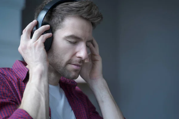 Jeune homme allemand heureux avec les yeux fermés écoutant de la musique dans les écouteurs à la maison avec le visage ravi — Photo