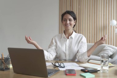 Huzurlu kadın serbest çalışan meditasyon yapan ve evde yoğun bir günün ardından nefes alma egzersizleri yapan.