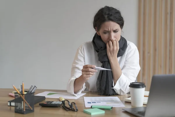 Unhappy latin business woman dressed in warm scarf checking body temperature at work — Foto Stock