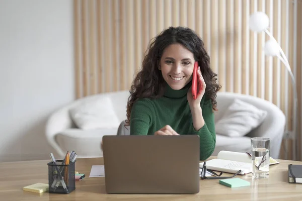 Feliz mujer de negocios italiana teniendo una agradable conversación de teléfono celular mientras trabaja en el ordenador portátil en casa —  Fotos de Stock