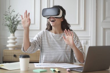Excited amazed woman wearing VR glasses enjoying amazing virtual reality experience at work