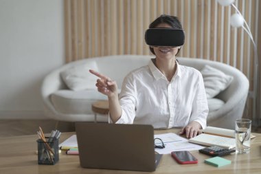 Female office worker in vr headset or virtual reality goggles touching objects in cyberspace