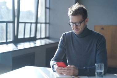 Ofiste masasında oturan ve akıllı telefon kullanan yakışıklı Alman iş adamı.