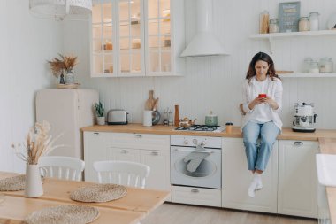 Mutlu genç bayanın telefonda mesajı var. Avrupalı ev hanımlarının boş vakitleri var ve evinde mutfaktaki atölyesinde oturuyorlar. Evde günlük kıyafetli bir kız. Modern lüks İskandinav iç mimarisi.