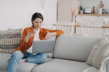 Genç İspanyol kadının evde online konferansı var. Bilgisayarlı kız internet toplantısında konuşuyor. Güzel bayan kanepede oturmuş tartışıyor. Karantina sırasında çalışıyor.