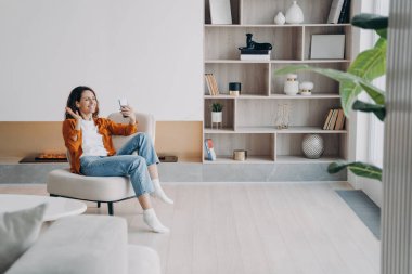 Hafta sonu sabahları keyif ve rahatlama. Mutlu Avrupalı kızın evde videosu var. Genç bir kadın kablosuz kulaklık kullanıyor ve telefonda arkadaşıyla konuşuyor. İletişim teknolojisi.