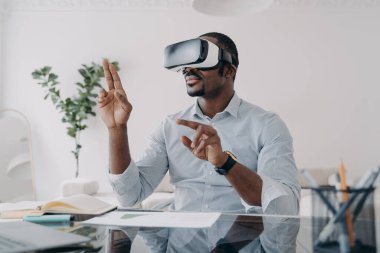VR kulaklıklı bir iş adamı sanal düğmelere basar. Freelancer tasarım projesi üzerinde çalışıyor. Evinde fütürist vr kulaklık takmış Afrikalı Amerikalı bir adam. İş ve yaratıcılık için modern dijital teknoloji.