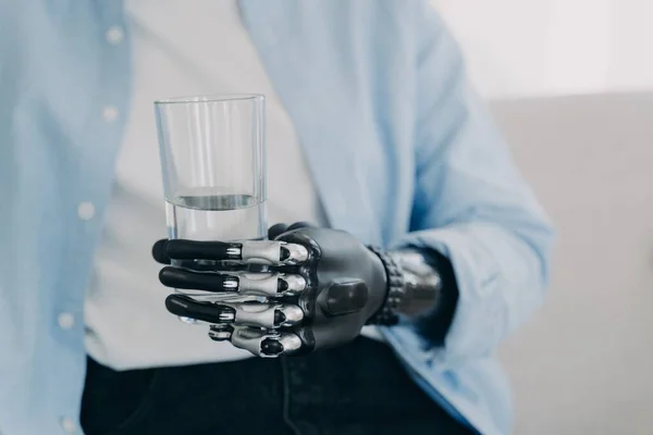 Morning routines of disabled person. Girl is using futuristic robotic arm prosthesis and holding glass of water at home. Modern bionic prosthesis. Healthy lifestyle after amputation surgery.