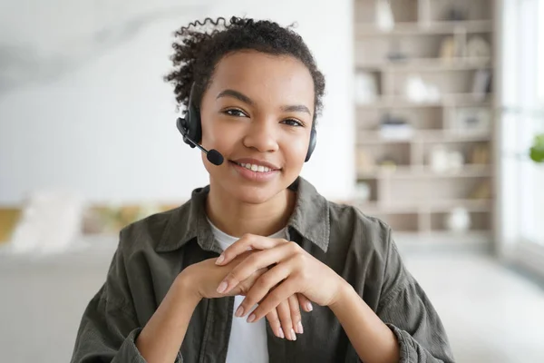 Virtual assistant. Young woman in headset gives consultation. Distance study on quarantine. Afro manager in earphones is smiling. Remote work of an operator of client support service from home.